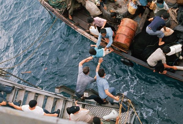 "South China Sea... Crewman of the amphibious cargo ship U.S.S. Durham (LKA-114) take Vietnamese refugees aboard from a small craft...."