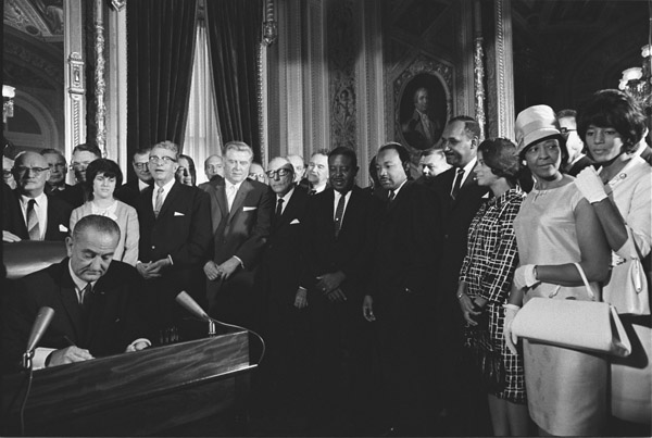 President Lyndon Johnson signs Voting Rights Act as MLK and others look on
