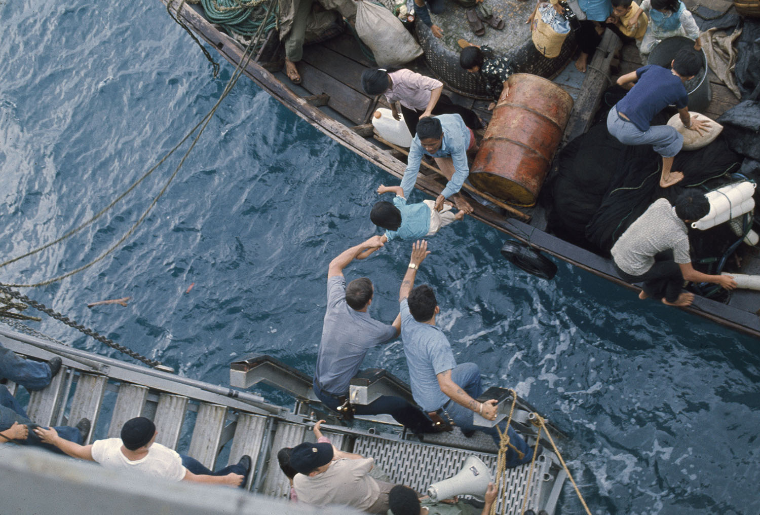 Crewmen of the amphibious cargo ship USS Durham take Vietnamese refugees from a small craft in the South China Sea, 1975