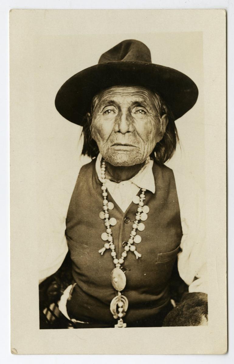 A photo of William Alchesay, probably taken when he was in his 70s. Alchesay is wearing a wide-brimmed hat, a squash blossom necklace, and a dark vest.