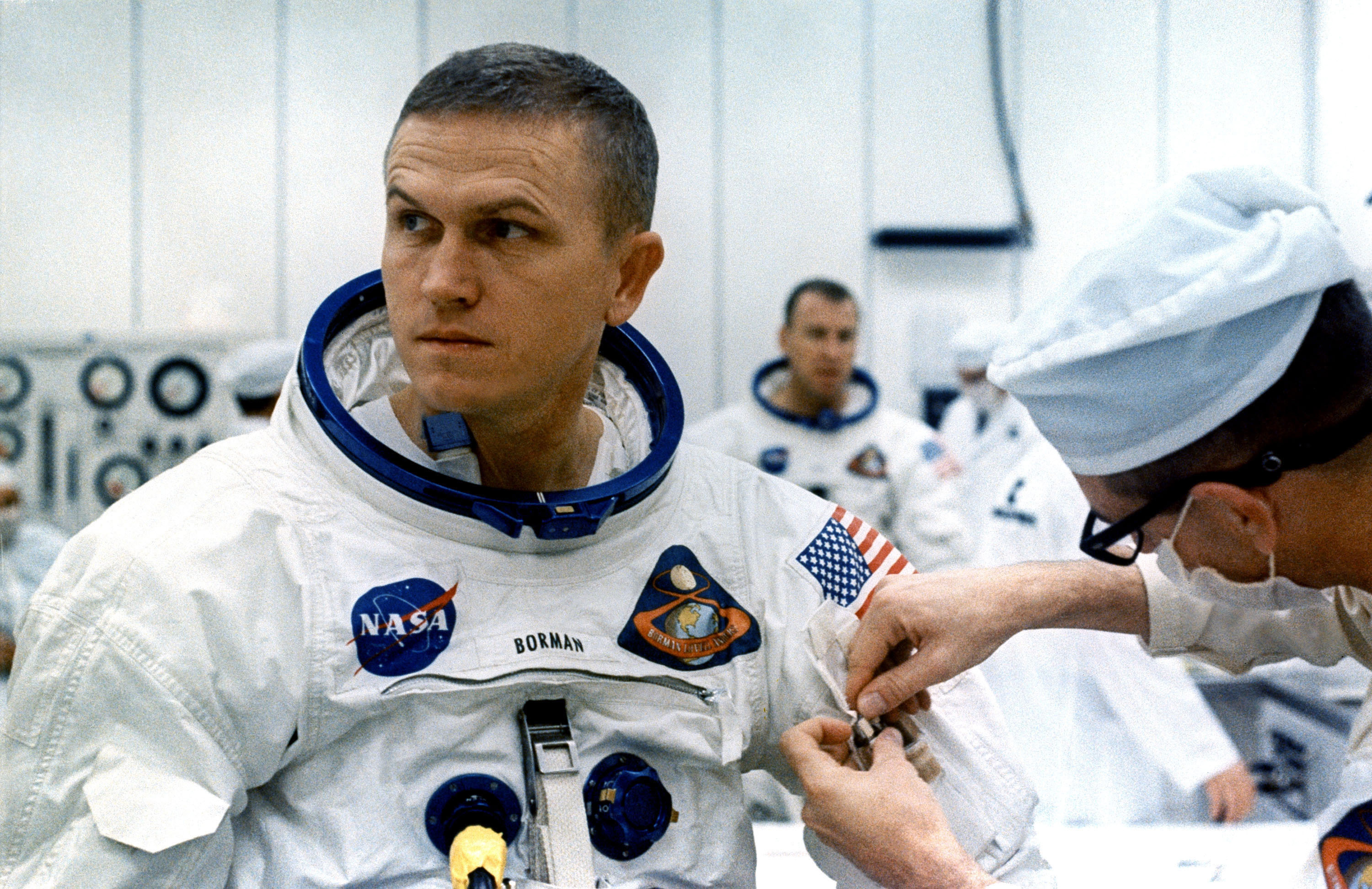 A technician places two inflight pens and a penlight in the spacesuit pocket of Apollo 8 commander Frank Borman
