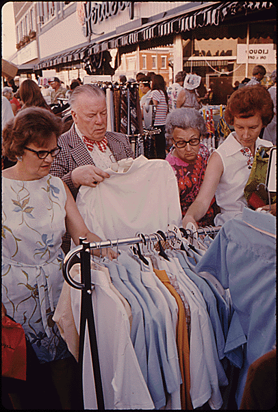 ADULTS LOOKING OVER BARGAIN MERCHANDISE PLACED IN THE STREET ON THE SIDEWALKS BY MERCHANTS IN NEW ULM, MINNESOTA