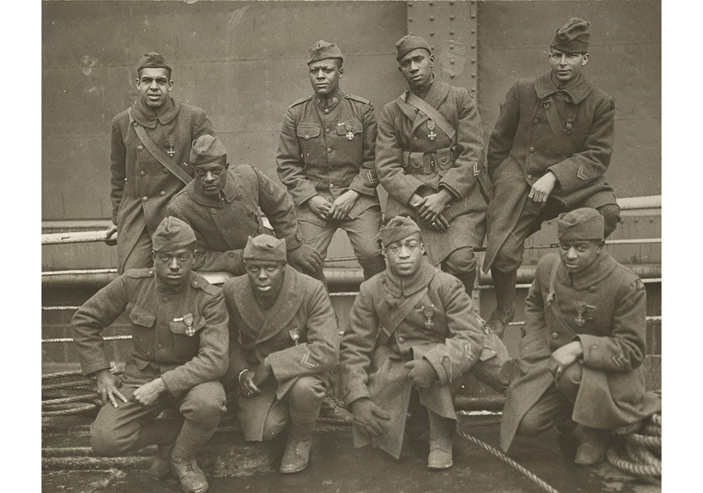 A sepia and white image of nine black men wearing uniforms, lined up in two rows