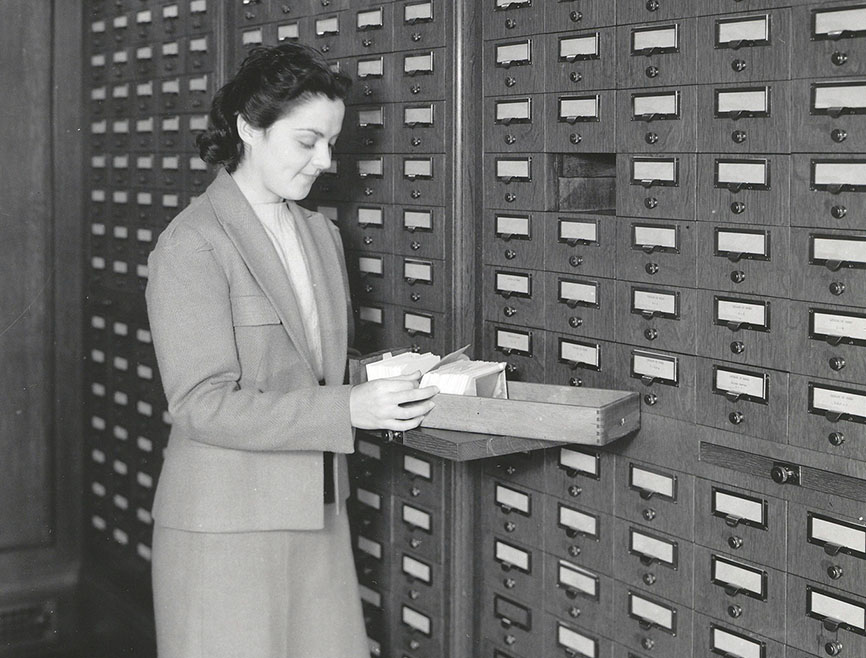 Woman looking through cards in an old-fashioned card catalog in a library, ca. 1940s