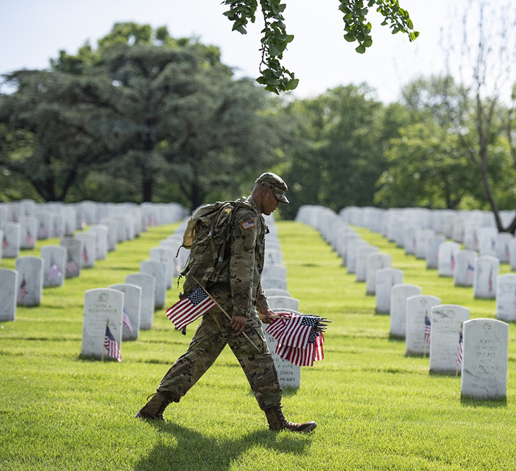 Soldier from 3rd Infantry Regiment placing flags on headstones in Arlington National Cemetery in preparation for Memorial Day 