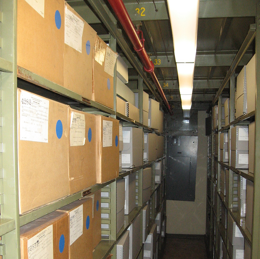 This view of the stacks shows the progress being made in rehousing records of the Immigration and Naturalization Service from large acidic cartons to smaller archival-quality storage boxes. 