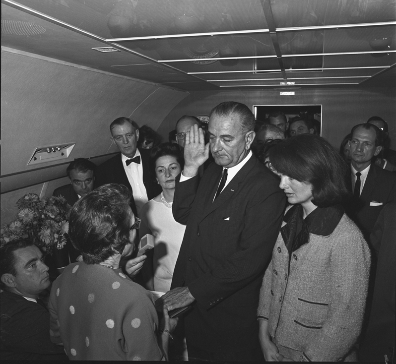 Aboard Air Force One, with Jacqueline Kennedy at his side, Lyndon Johnson is sworn in as President 