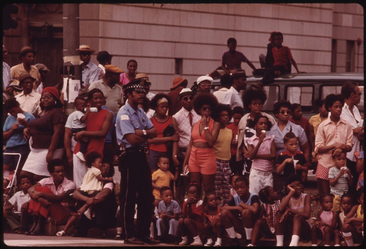 crowd of Black people standing on the side of a street watching parade 