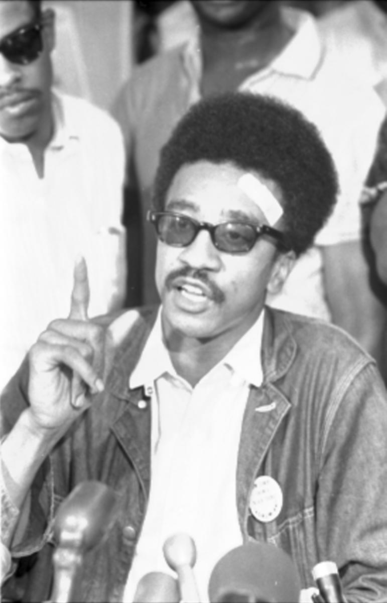 half-length portrait of Brown (later Jamil Al-Amin) speaking into a microphone with a bandage on his forehead