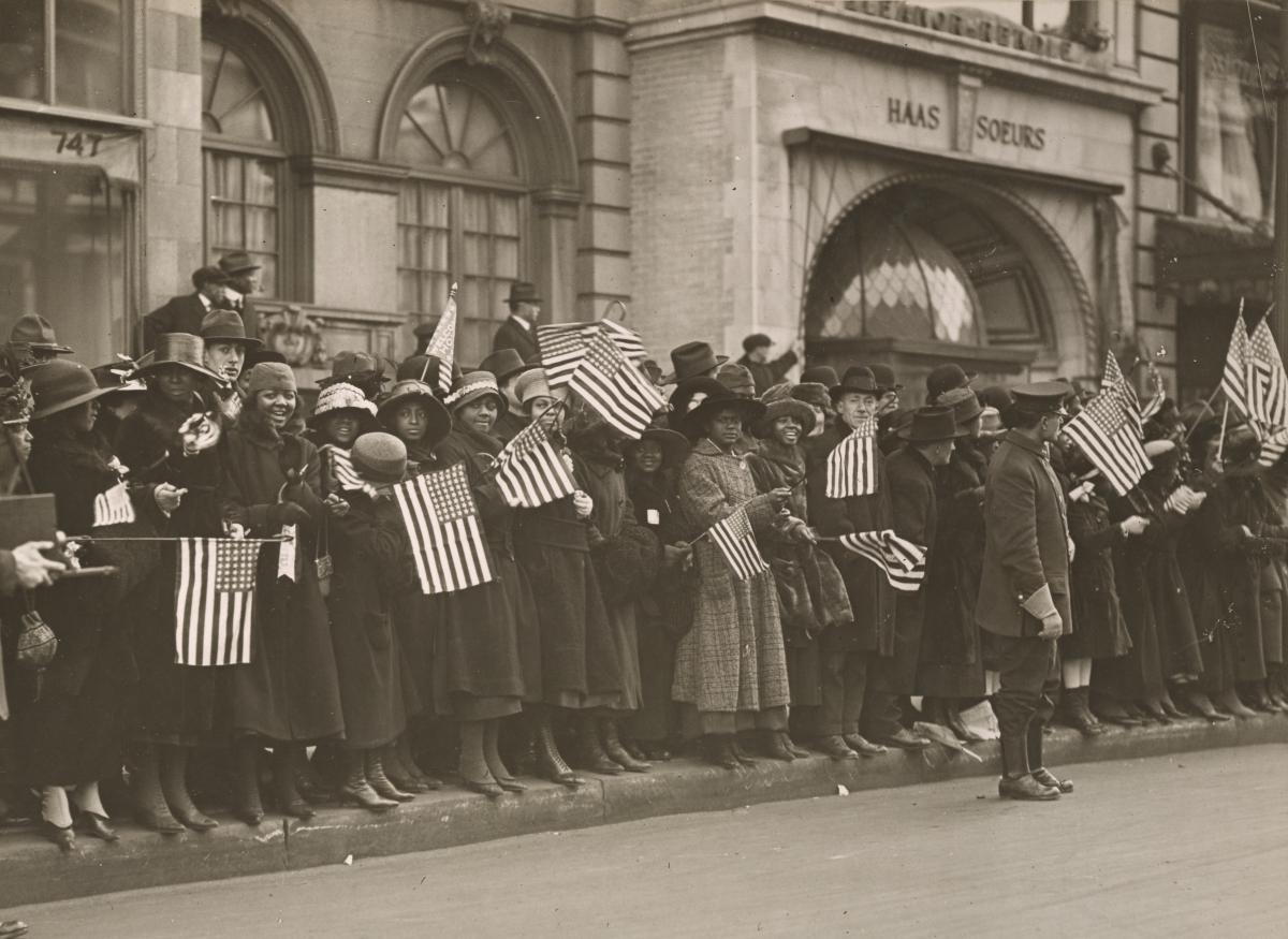 people lined on the side of a street waving American flags
