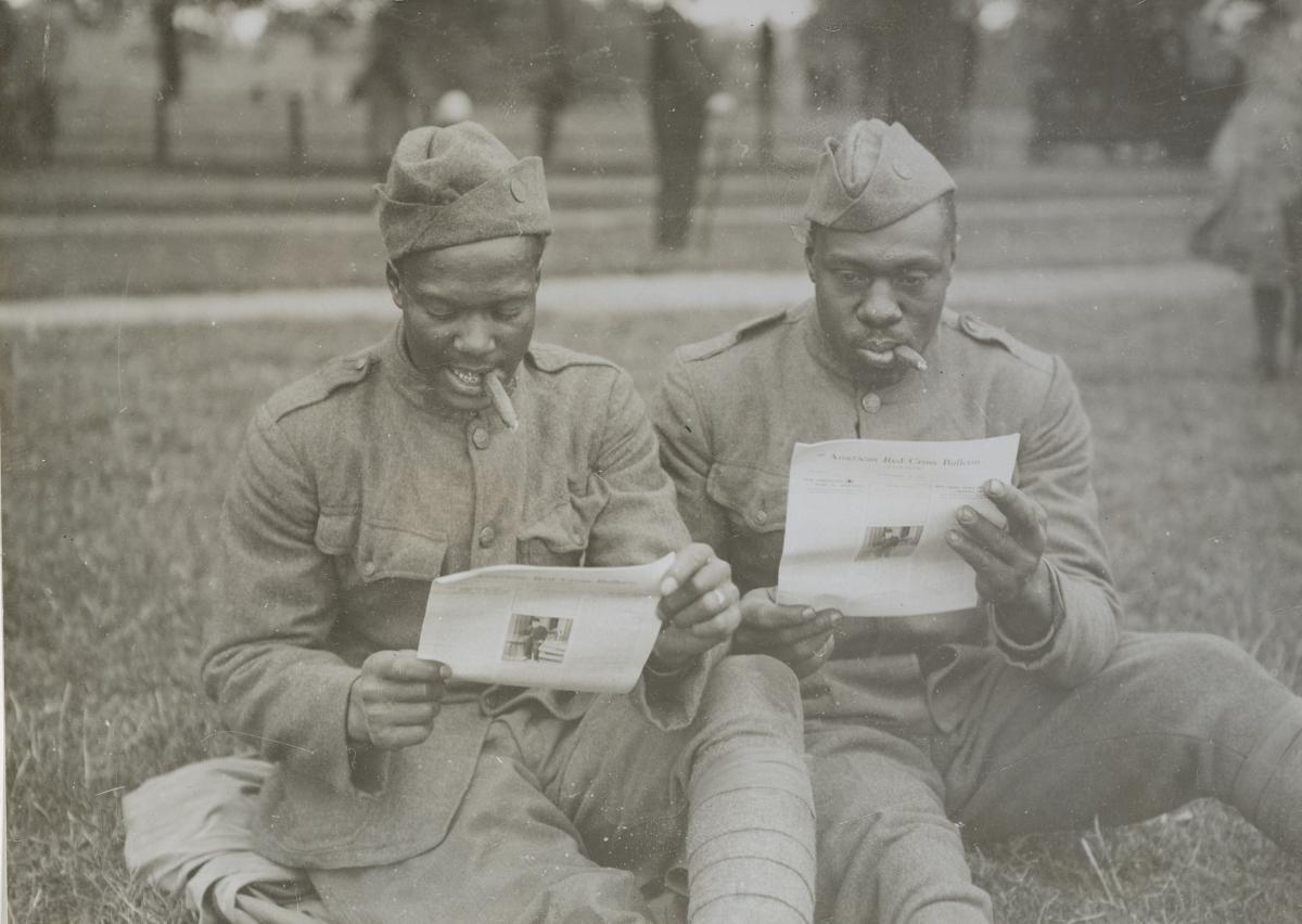 2 soldiers sitting in the grass reading a Bulletin