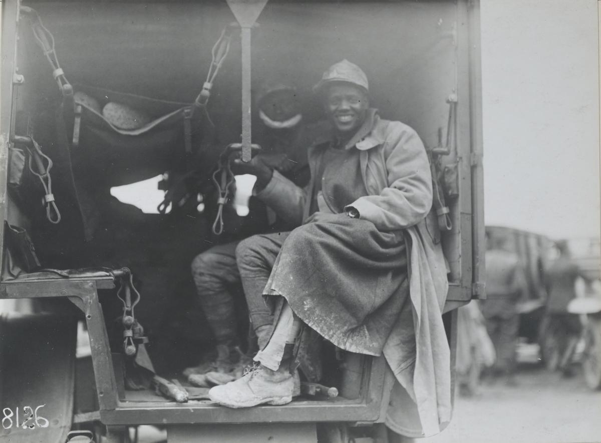 man sitting on the back of a truck, dressed in a long coat, smiling at camaera
